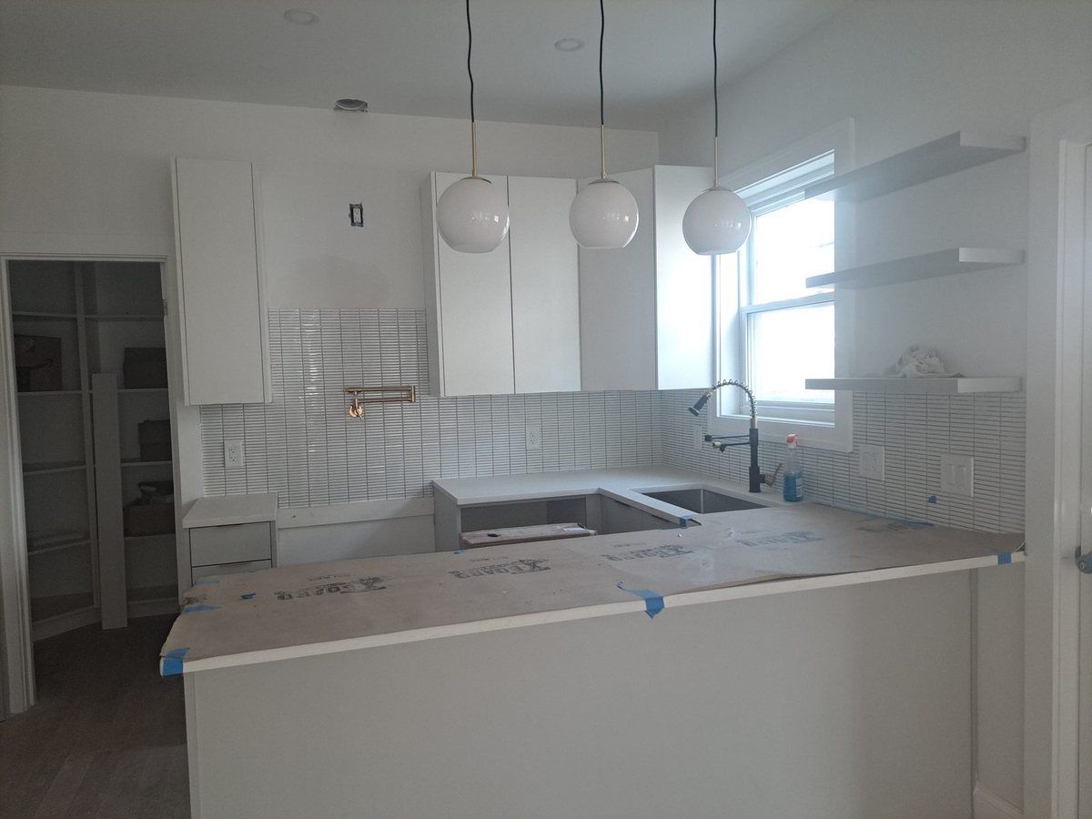 Kitchen under renovation with white cabinets, subway tile backsplash, three pendant lights and countertops covered with protective paper