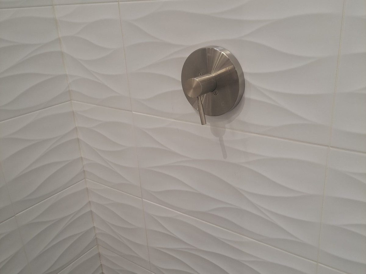 Shower wall with white 3D wave tile and a brushed-nickel valve trim